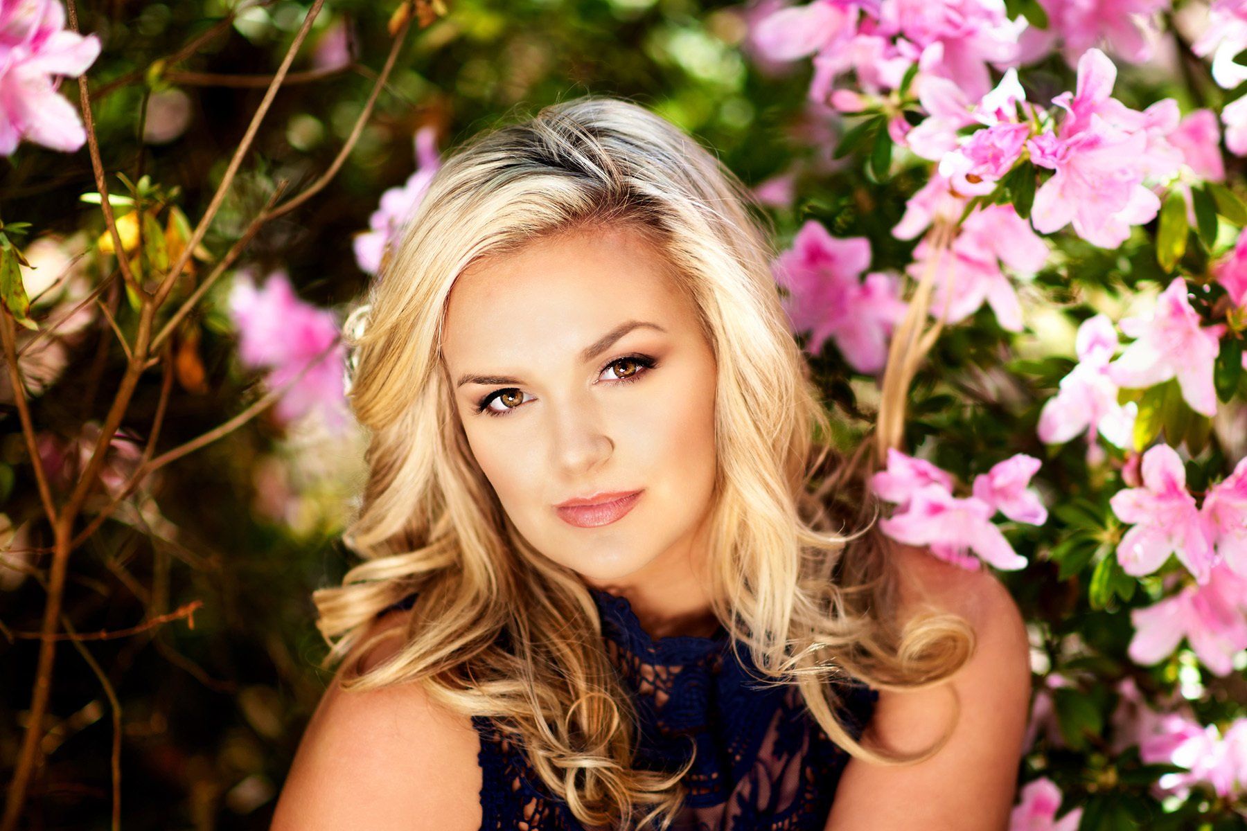 A woman is sitting in front of a bush of pink flowers.
