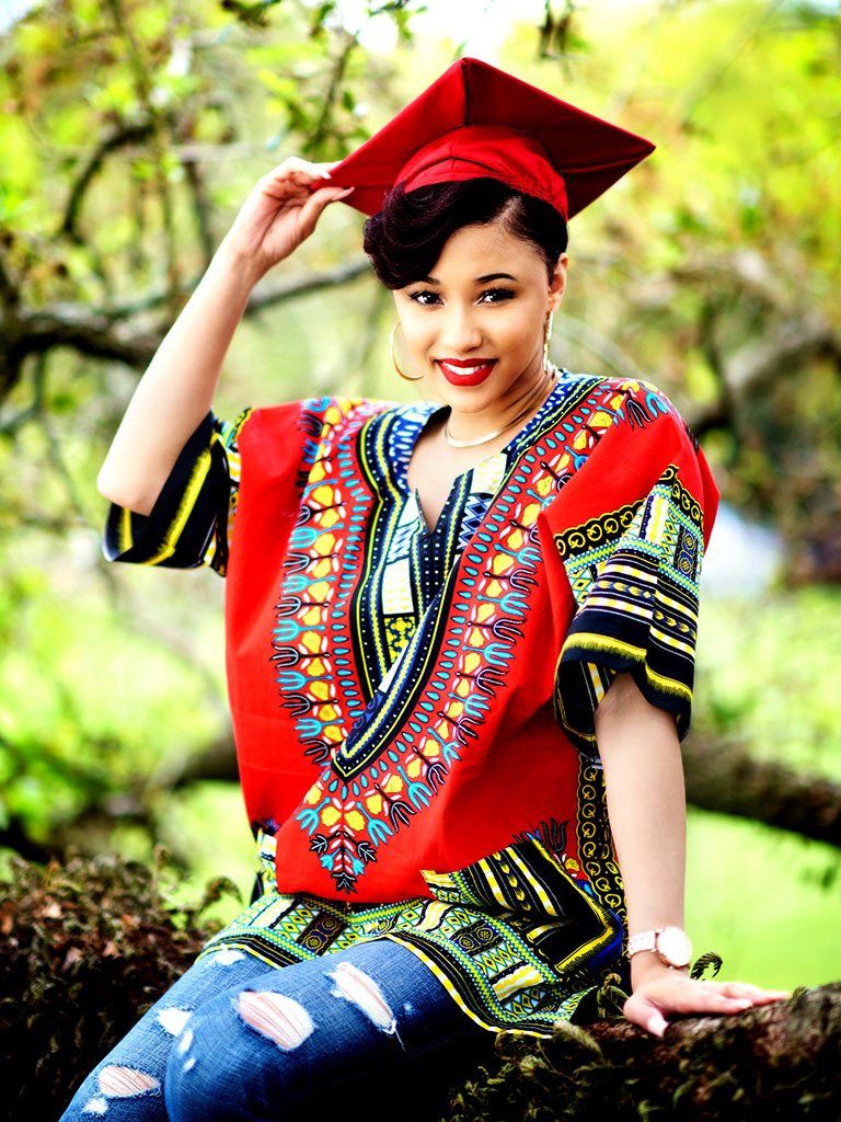 A woman wearing a graduation cap and gown is sitting on a tree branch.
