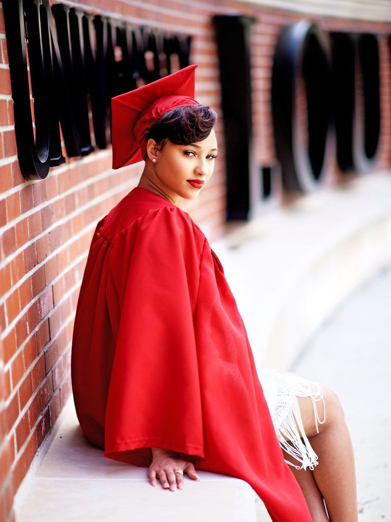 A woman in a red cap and gown is sitting on a bench.