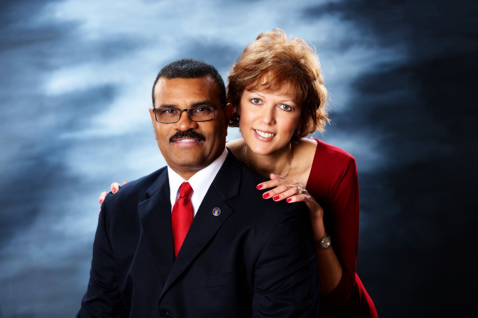 A man and woman are posing for a picture and the woman is wearing a red dress.