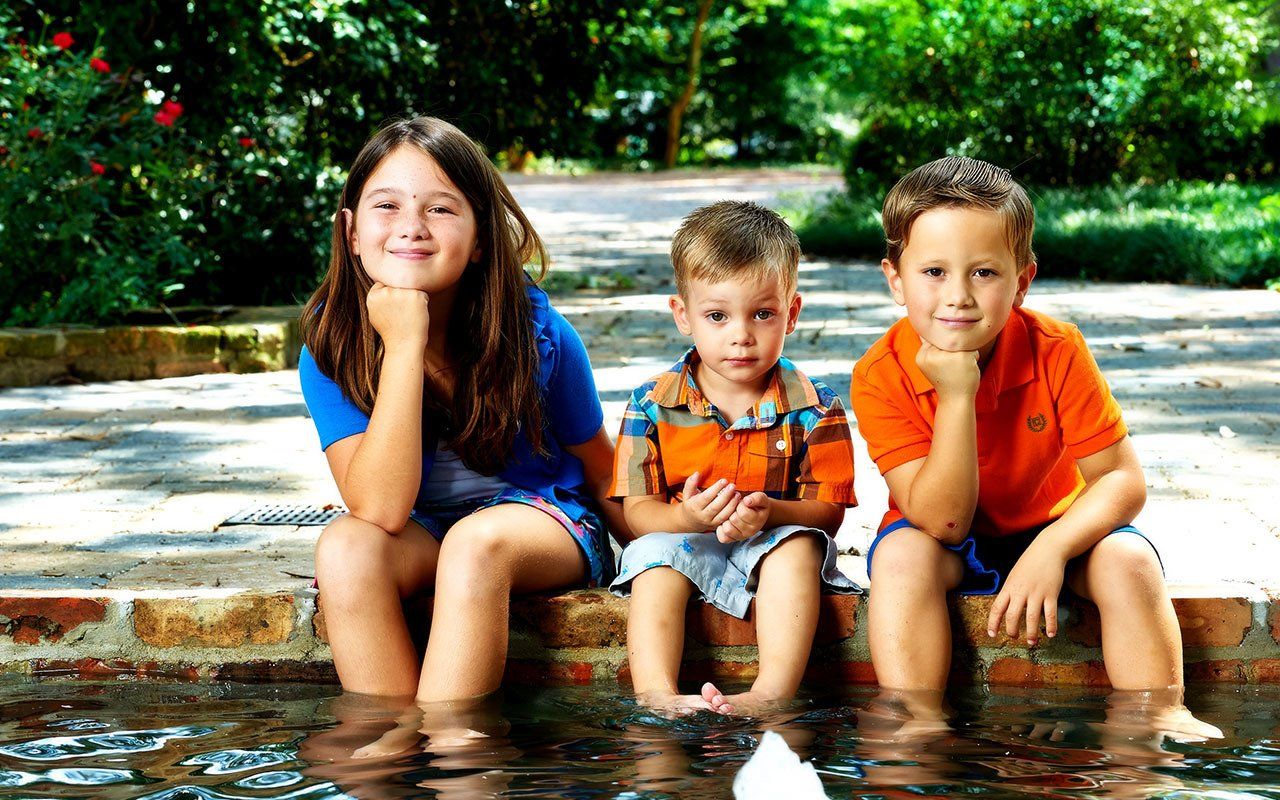 Three children are sitting in a pool of water with their feet in the water.