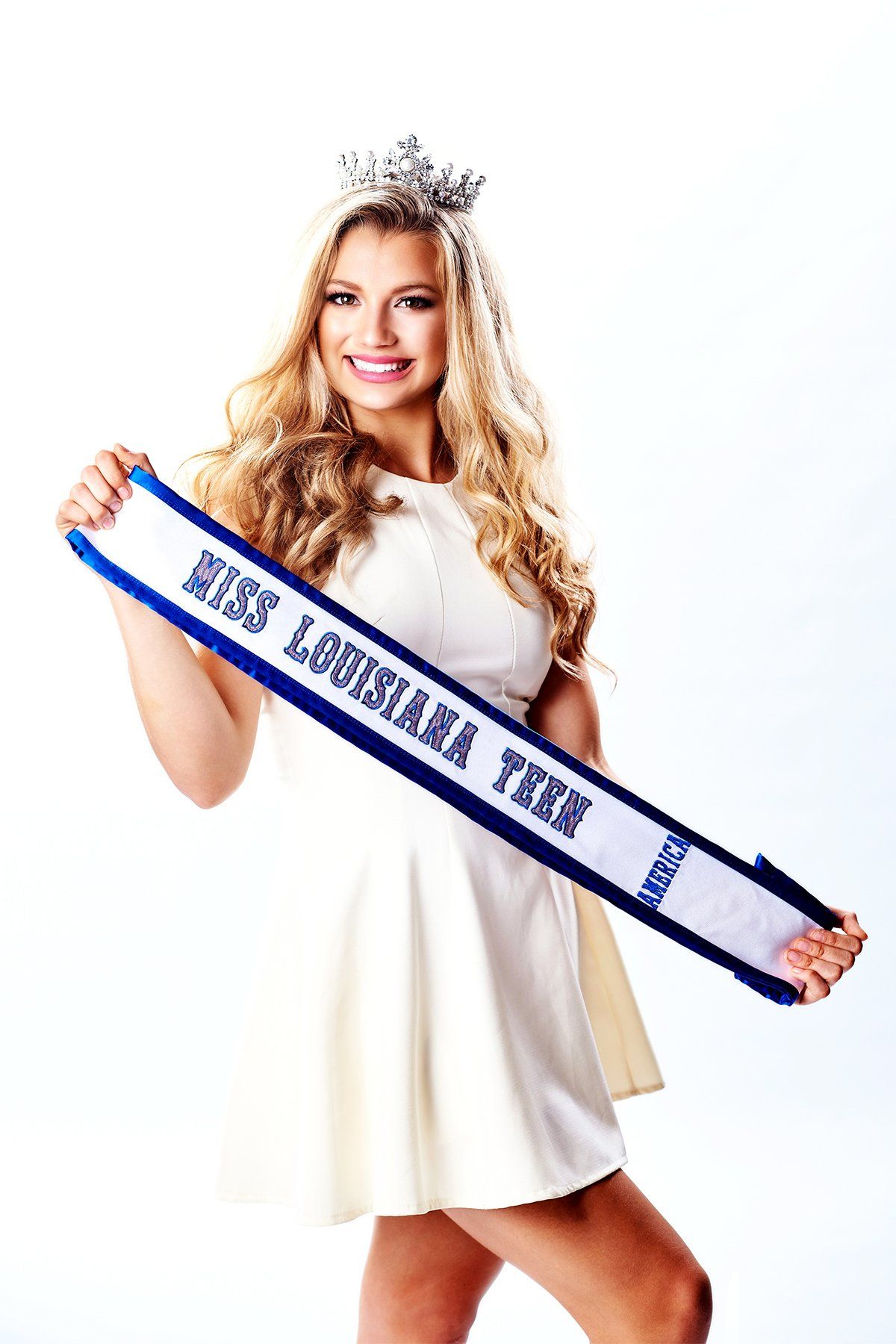 A woman in a white dress is holding a sash that says miss louisiana teen.