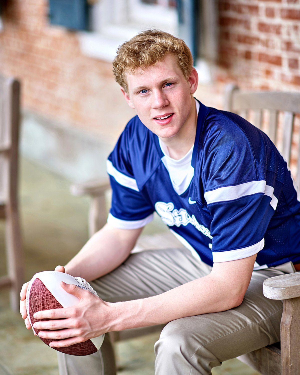 A young man in a blue jersey is sitting on a bench holding a football