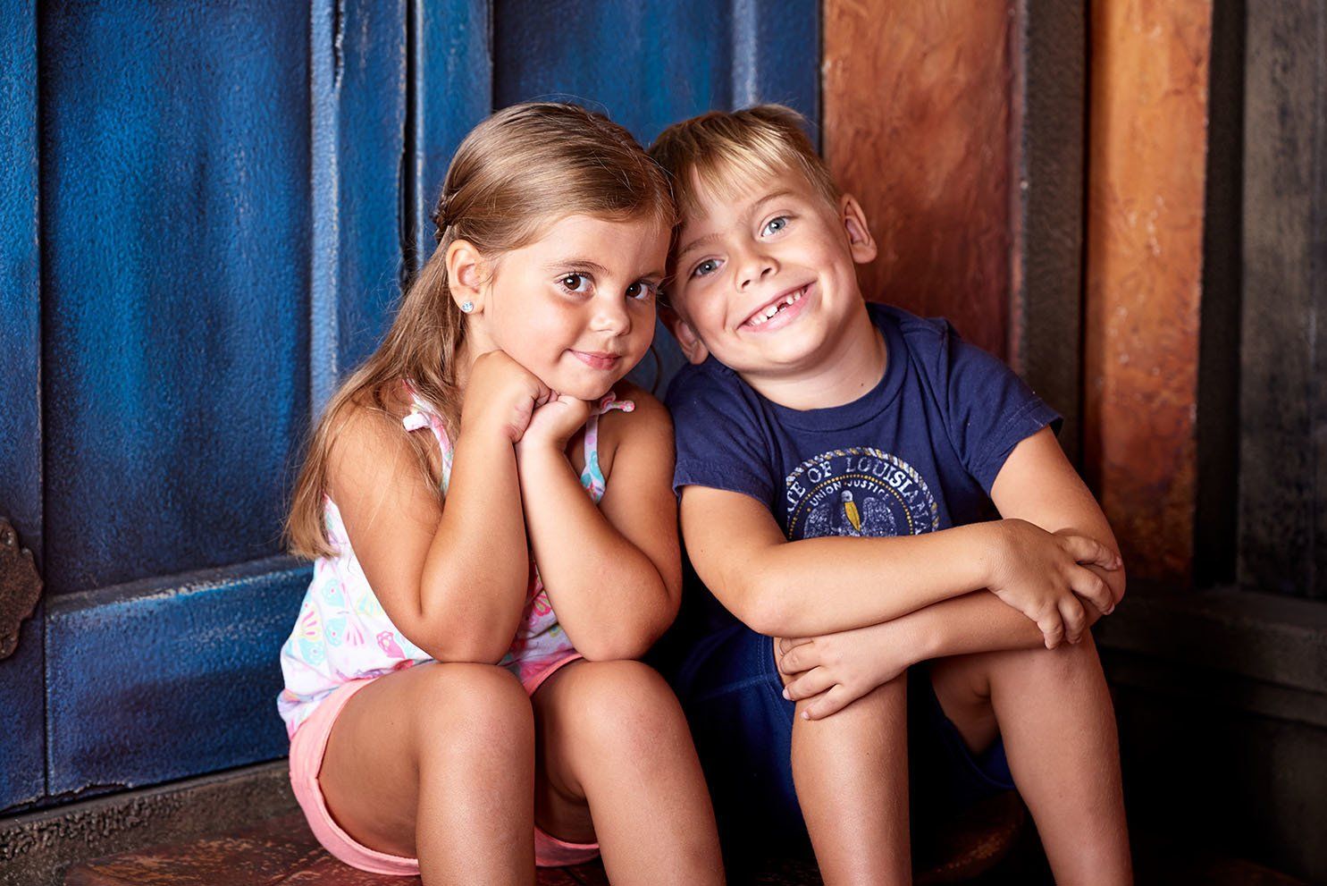 A boy and a girl are sitting next to each other in front of a blue door.