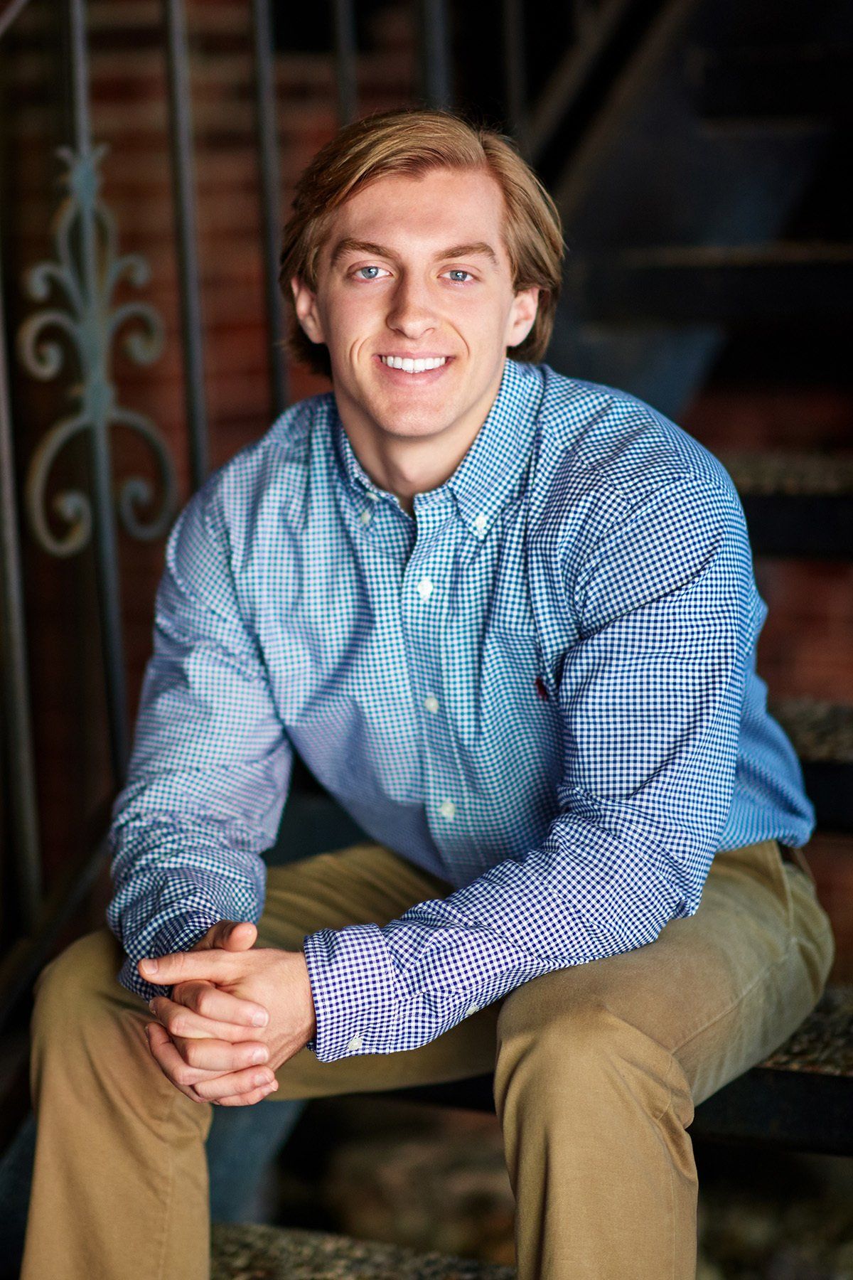 A young man is sitting on a set of stairs with his hands folded and smiling.