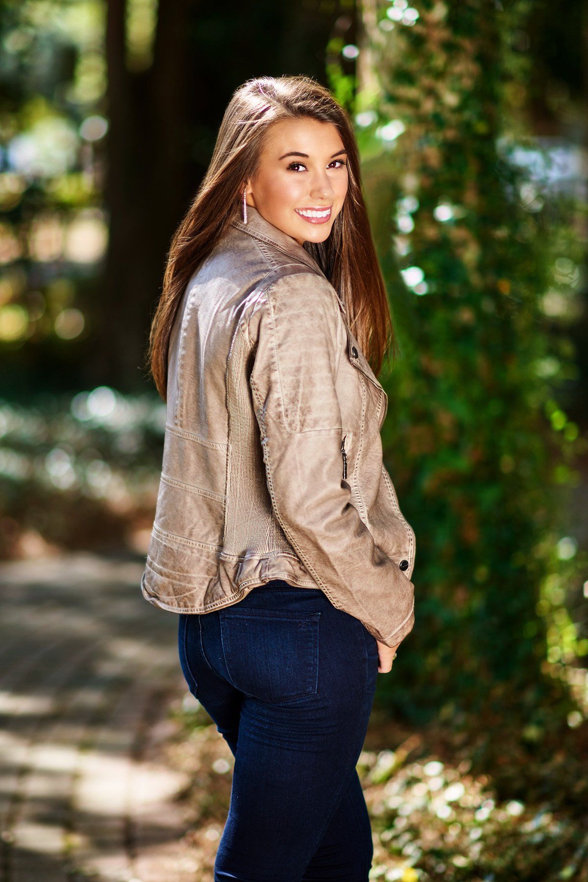 A young woman in a leather jacket and jeans is standing in the woods.