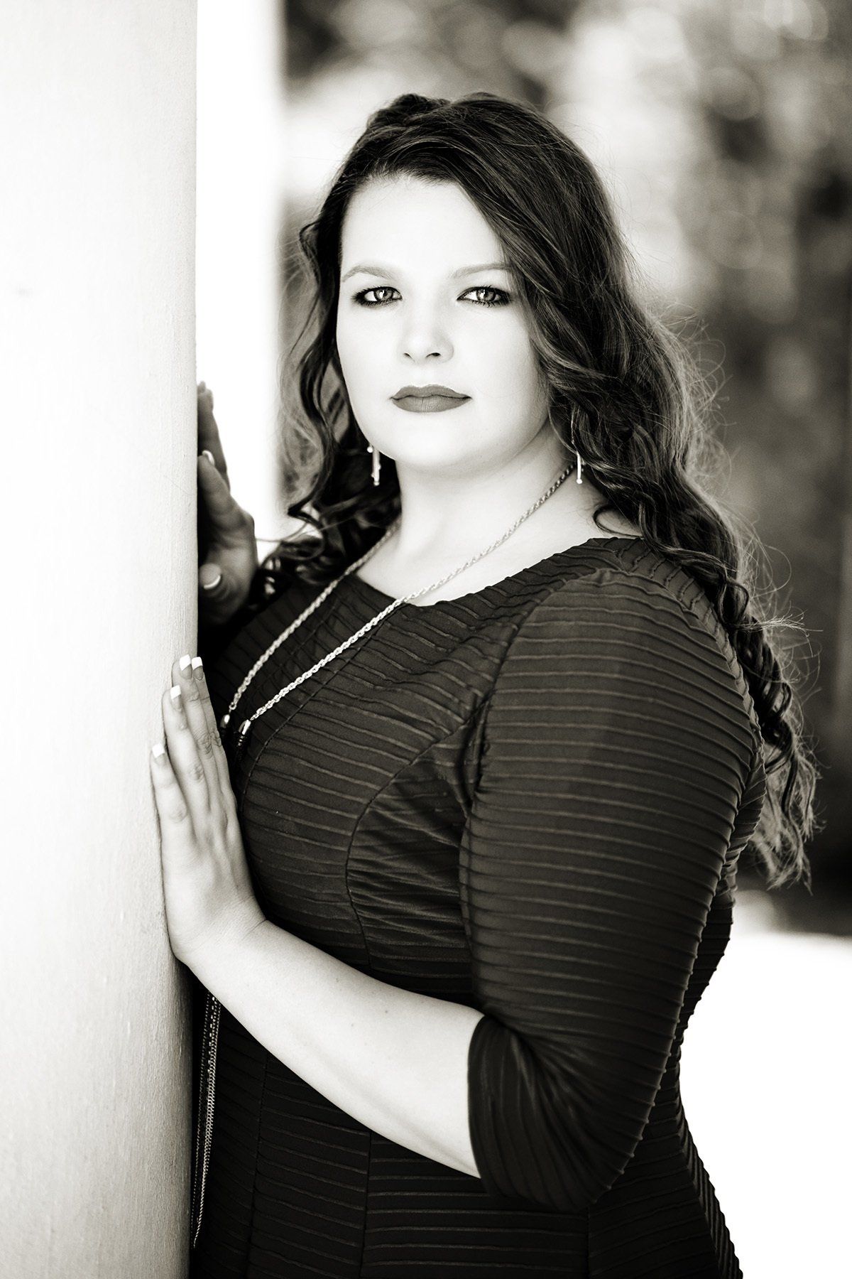 A black and white photo of a woman leaning against a wall.