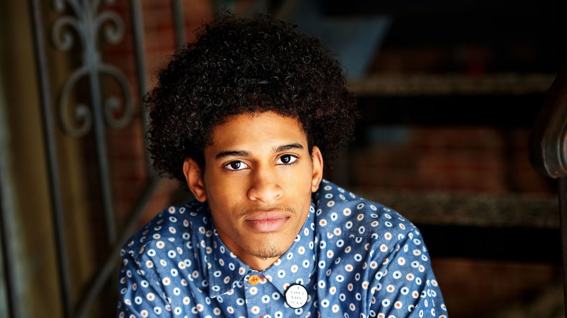 A young man with curly hair is sitting on a set of stairs.