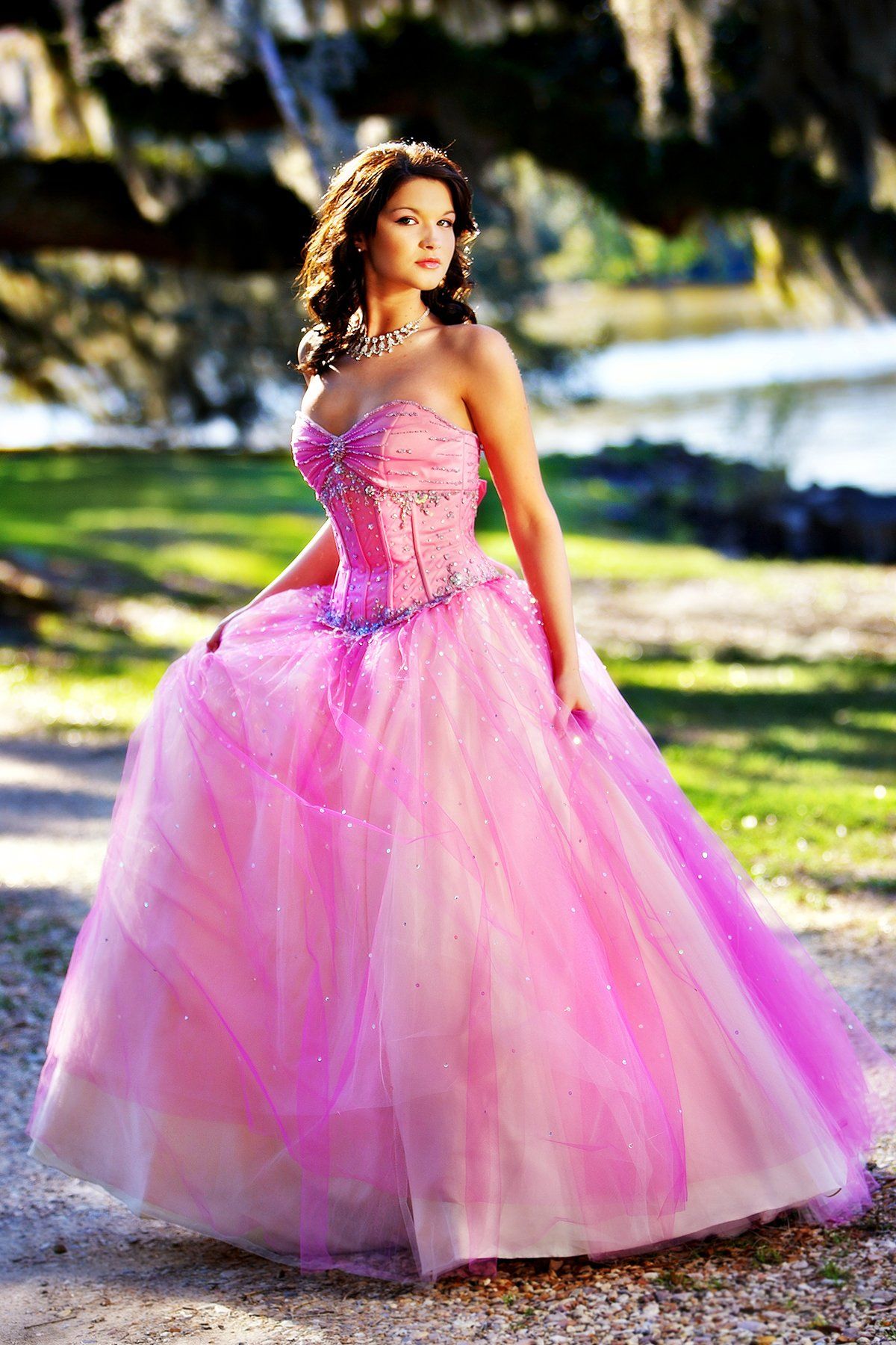 A woman in a pink ball gown is standing in a park.
