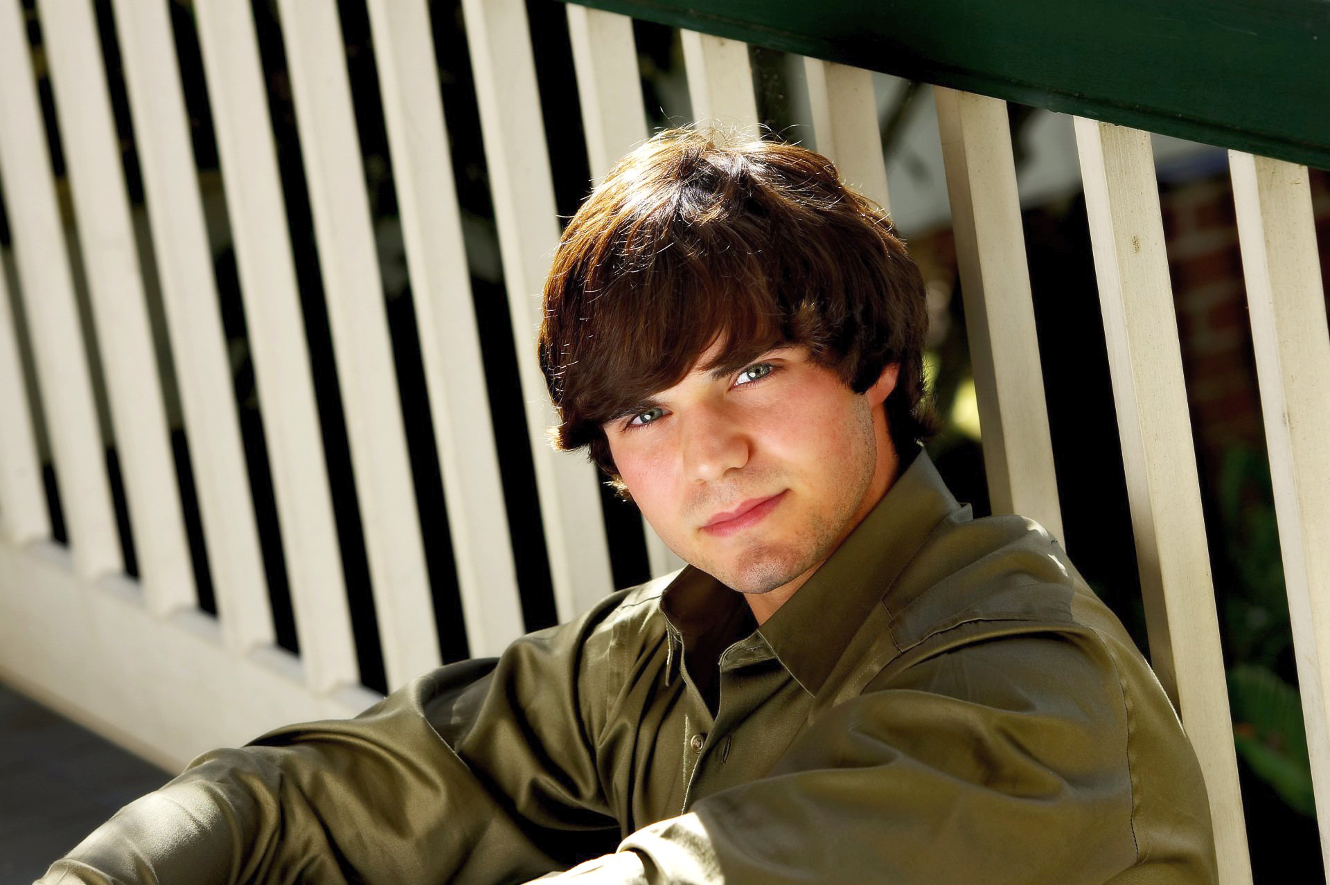 A young man in a green shirt is sitting on a porch railing