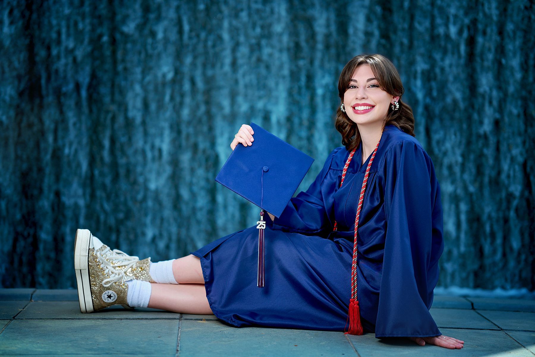 A young girl in a white dress is tying her ballet shoes while sitting on a bench.