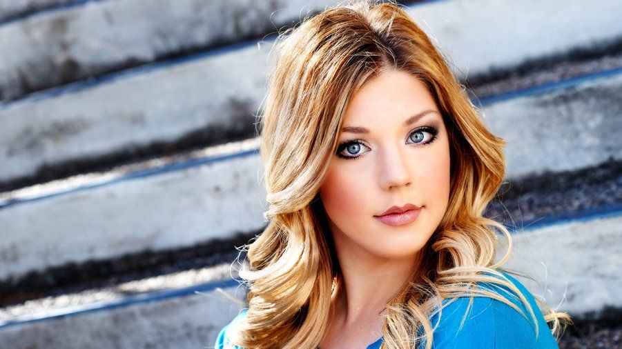 A woman in a blue shirt is standing in front of a set of stairs.
