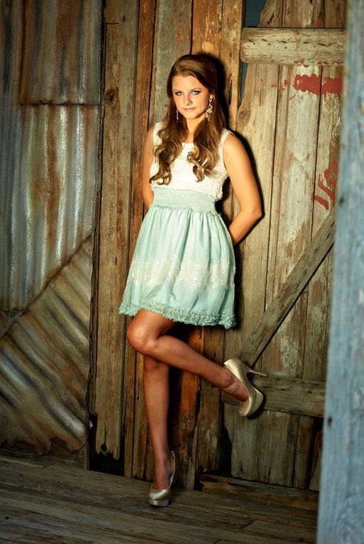 A woman in a blue dress is leaning against a wooden wall.