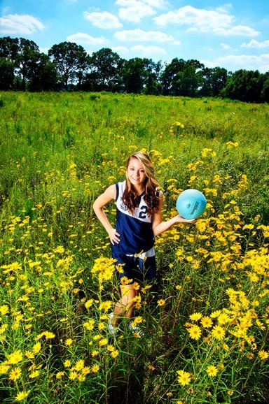 A girl is holding a soccer ball in a field of yellow flowers.