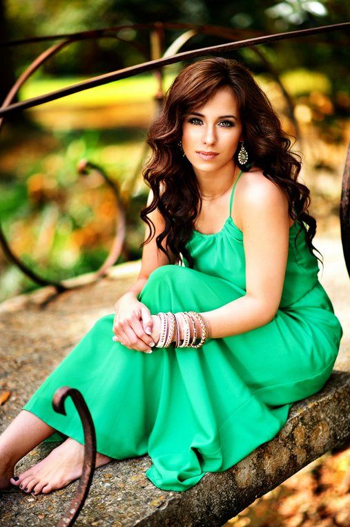 A woman in a green dress is sitting on a rock.