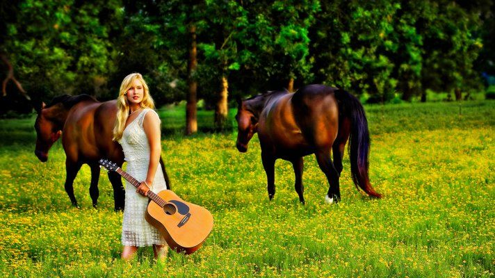 A woman is holding a guitar in a field with two horses.