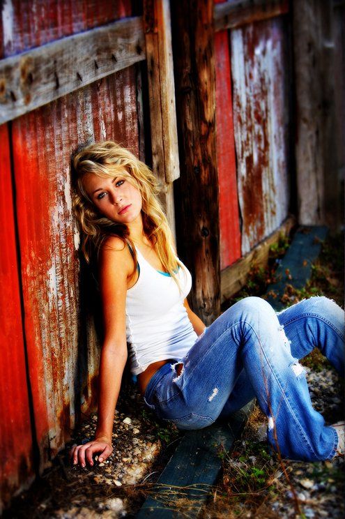 A woman is sitting on the ground leaning against a red barn door.