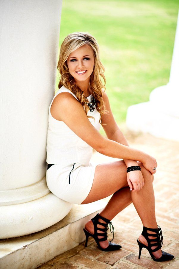 A woman in a white dress and black heels is sitting on a pillar.
