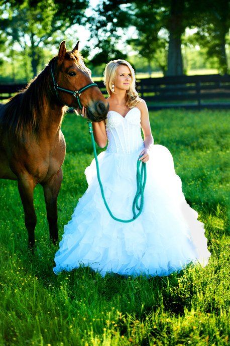 A woman in a wedding dress is standing next to a horse in a field.