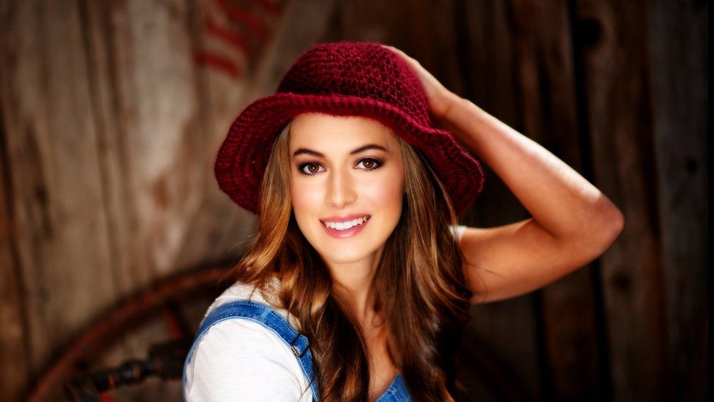 A woman wearing a red hat and overalls is smiling.