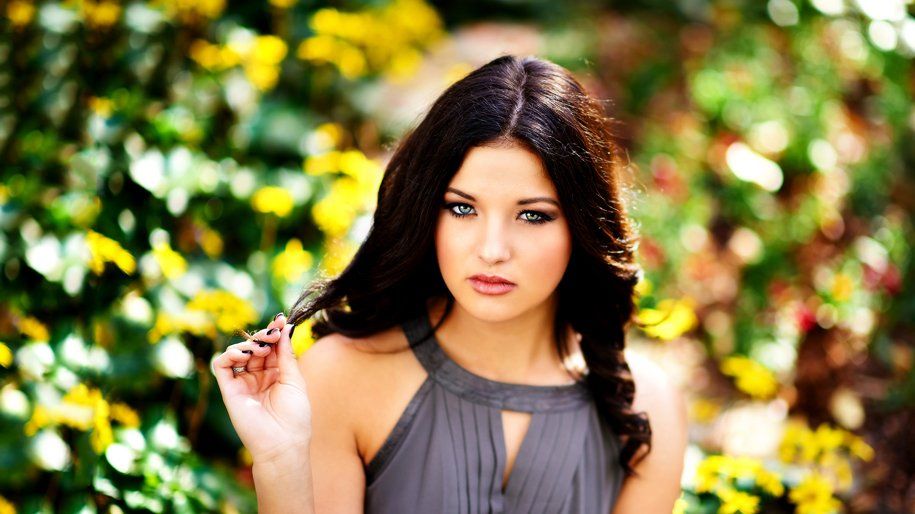A woman in a gray dress is standing in front of a bush with yellow flowers.