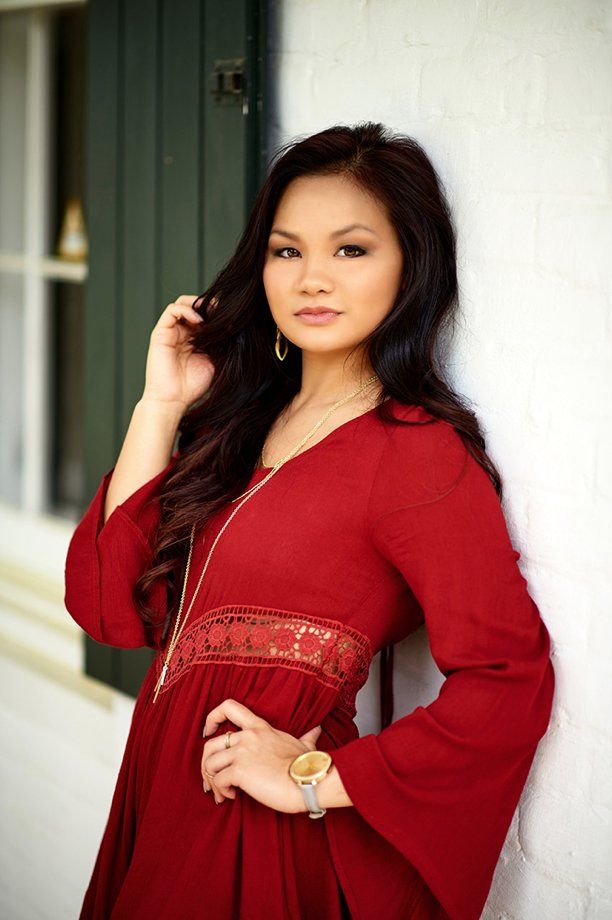 A woman in a red dress is leaning against a white wall.
