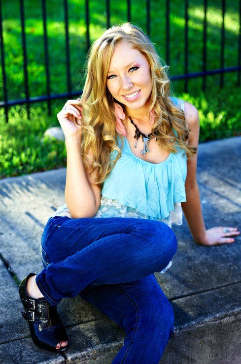 A woman in a blue tank top and blue jeans is sitting on a sidewalk.