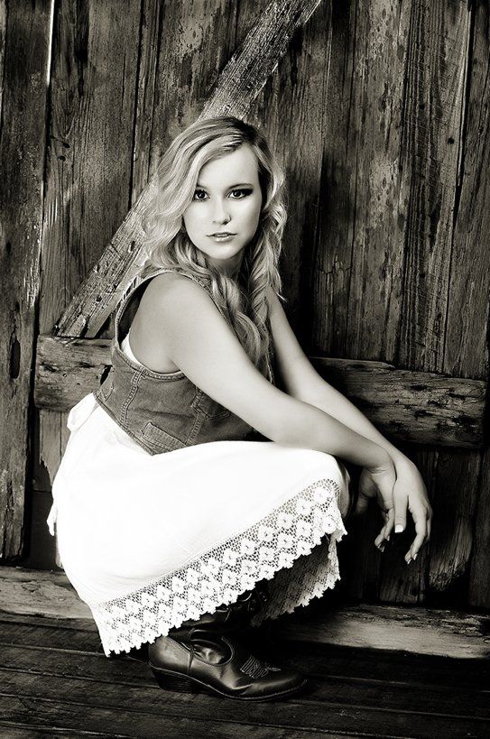A woman is squatting down in front of a wooden wall in a black and white photo.