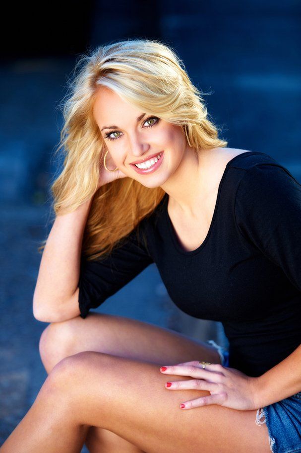 A woman is sitting on the ground with her legs crossed and smiling.