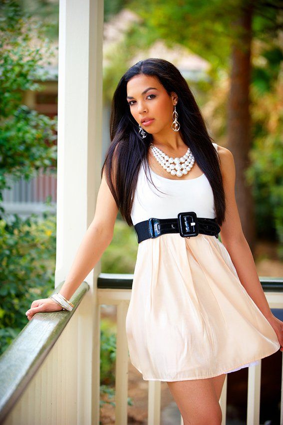 A woman in a white dress and pearl necklace is standing on a porch.