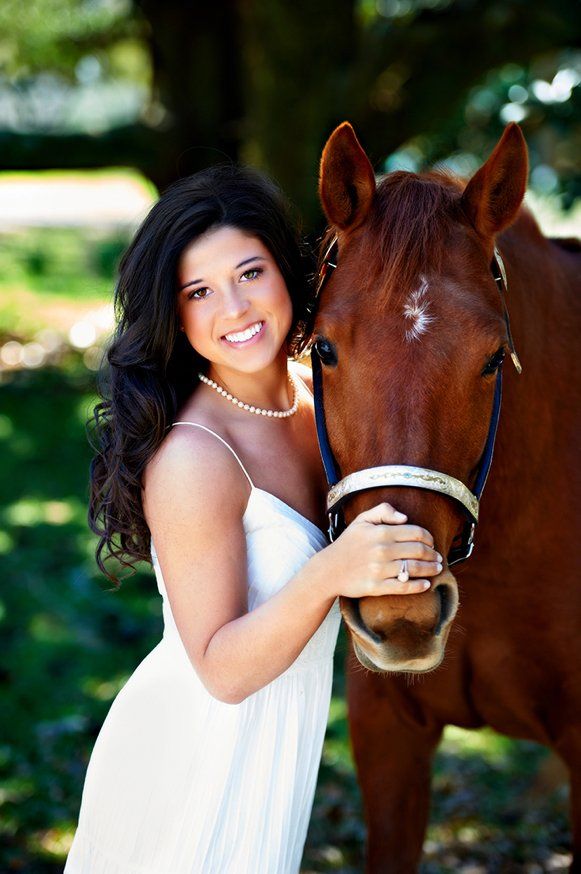 A woman in a white dress is standing next to a brown horse.