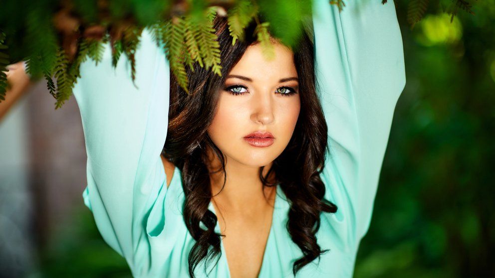A woman in a blue dress is standing under a tree with her arms outstretched.