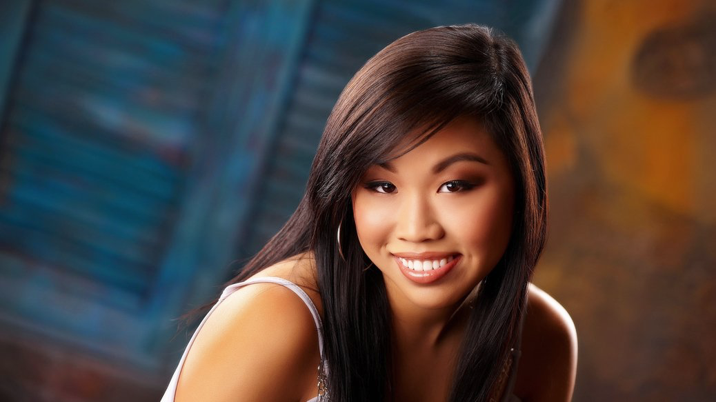 A woman with long dark hair is smiling and looking at the camera.