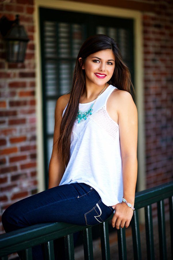 A woman is sitting on a railing in front of a brick building.