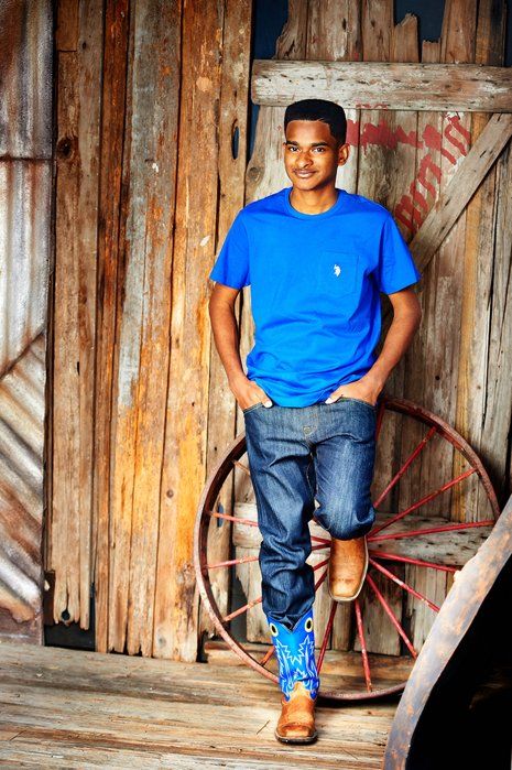 A young man in a blue shirt is standing next to a wagon wheel.