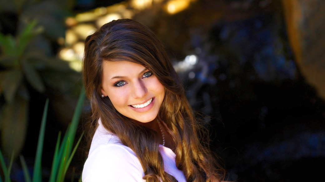 A young woman is smiling for the camera in front of a waterfall.