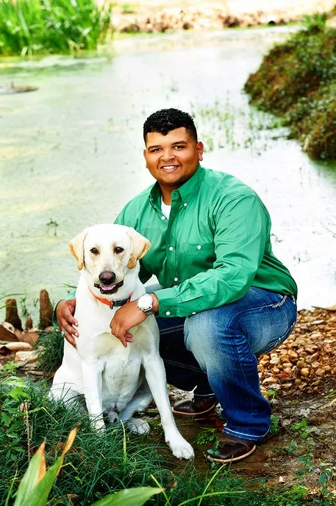 A man in a green shirt is kneeling down next to a white dog