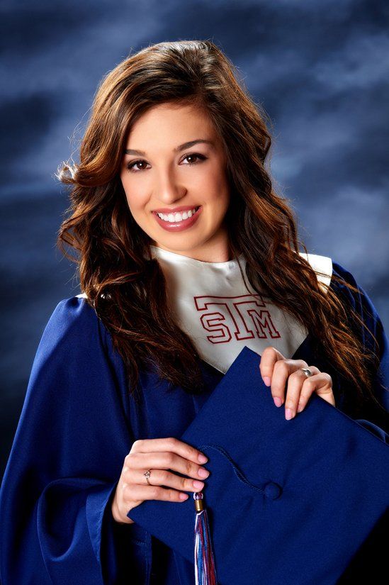 A woman in a graduation cap and gown is smiling and holding her cap
