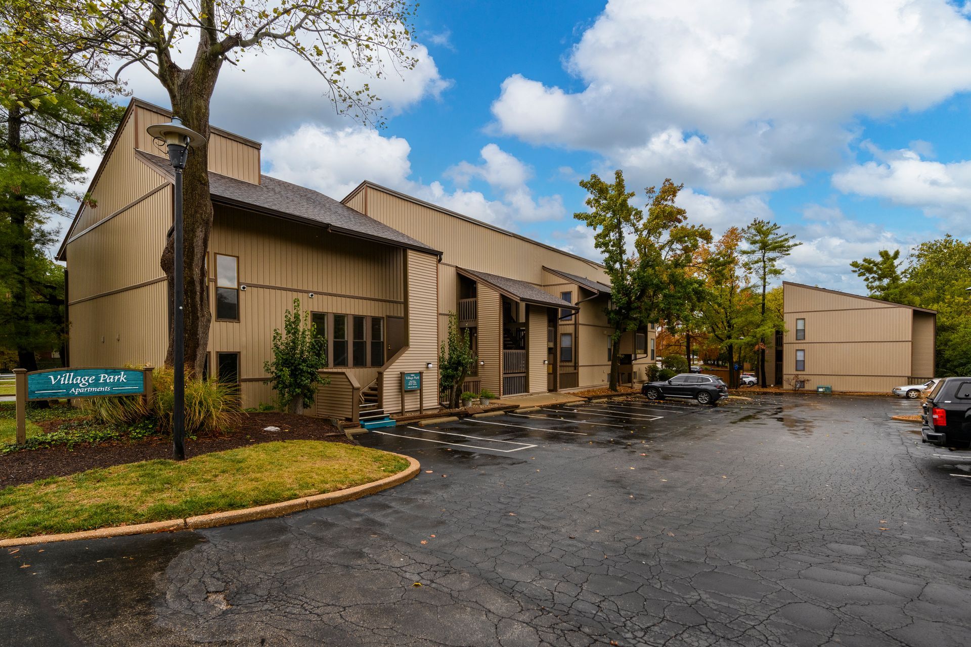 Tan multi-unit building with dark asphalt parking area, blue sky.