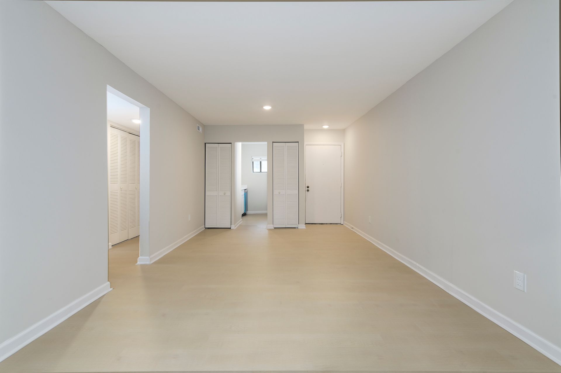 Empty, rectangular room with light walls and flooring. Doors lead to other rooms.