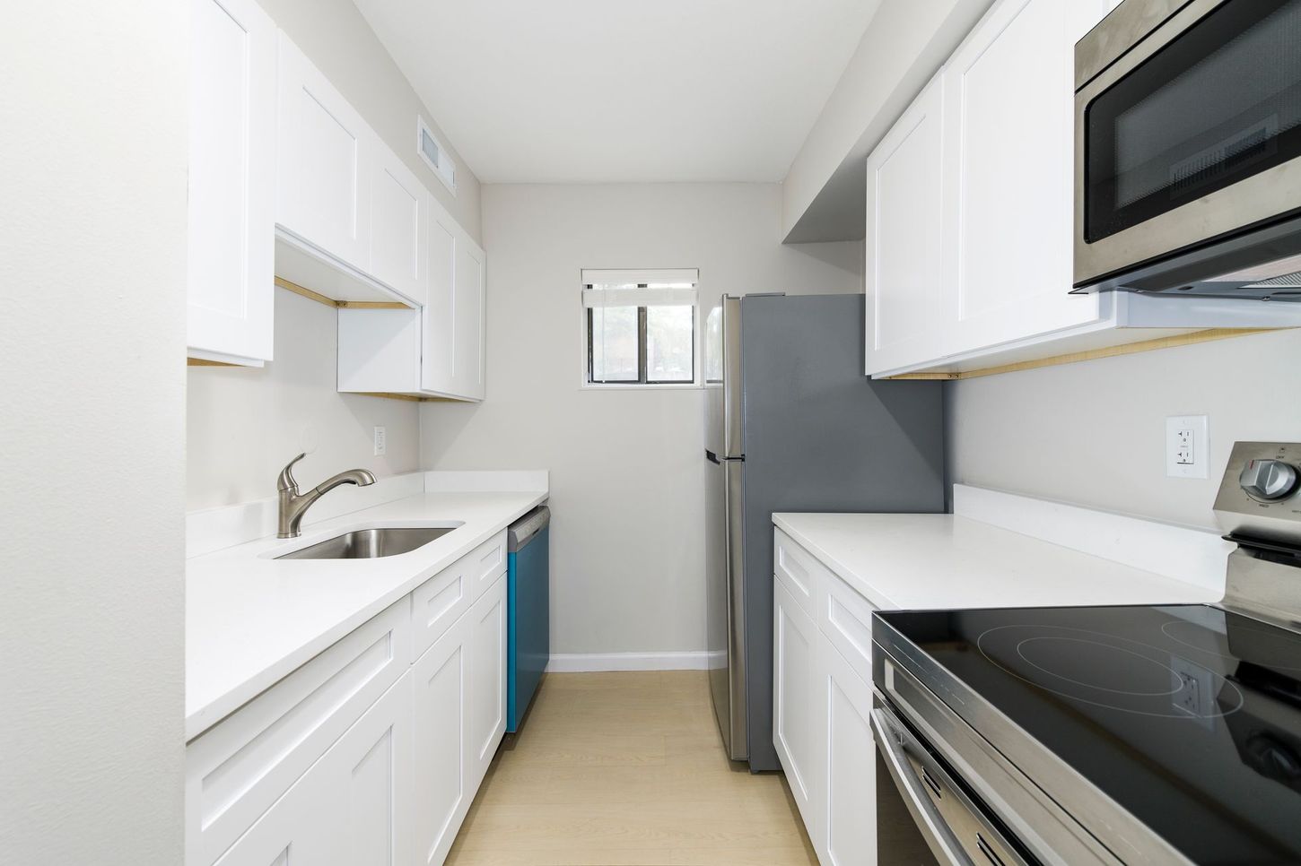 White kitchen with white cabinets and countertops, a stainless steel microwave and stove, and a blue dishwasher.