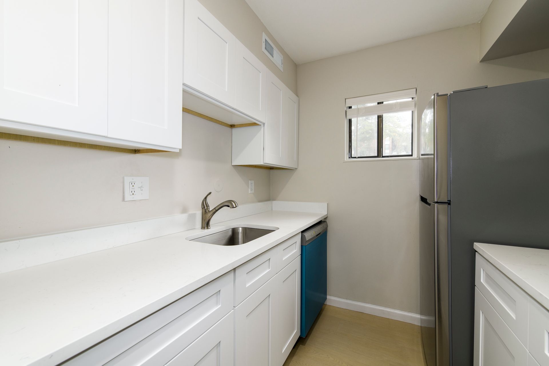 White kitchen with cabinets, countertops, stainless steel sink, blue dishwasher, and gray refrigerator.