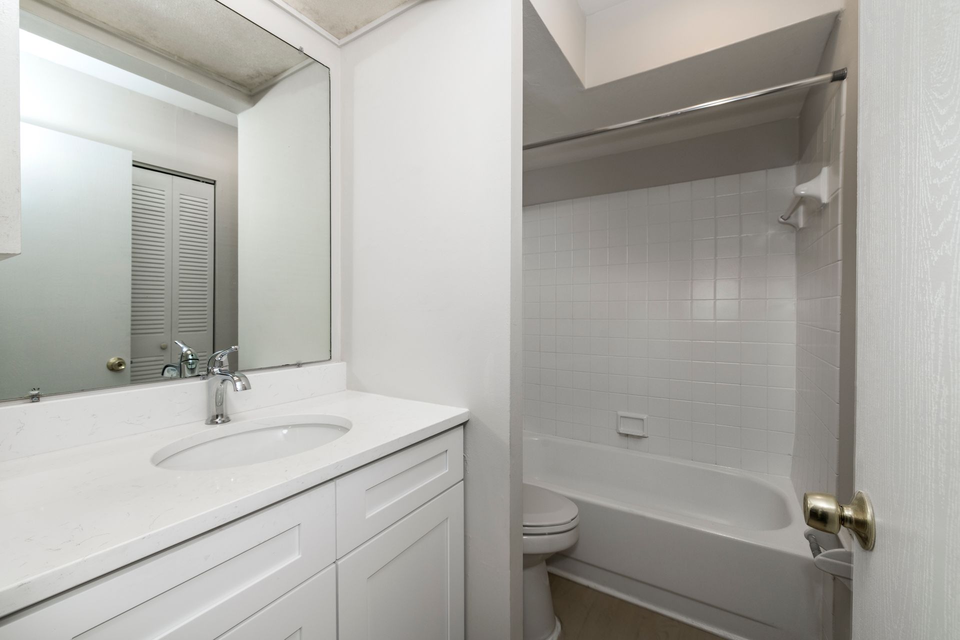 White bathroom with a vanity, sink, mirror, and a tub/shower combination.