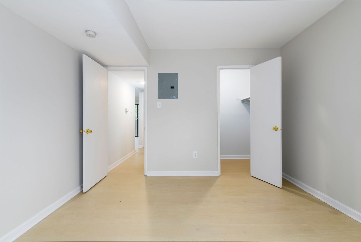 Empty room with two open doors and a hallway. Pale wood floors, gray walls.