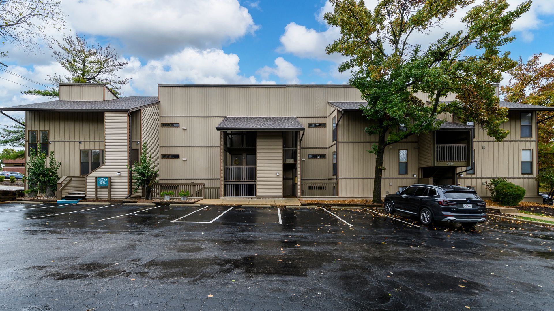 Exterior view of a two-story beige apartment building with a parking lot and a car parked in front.