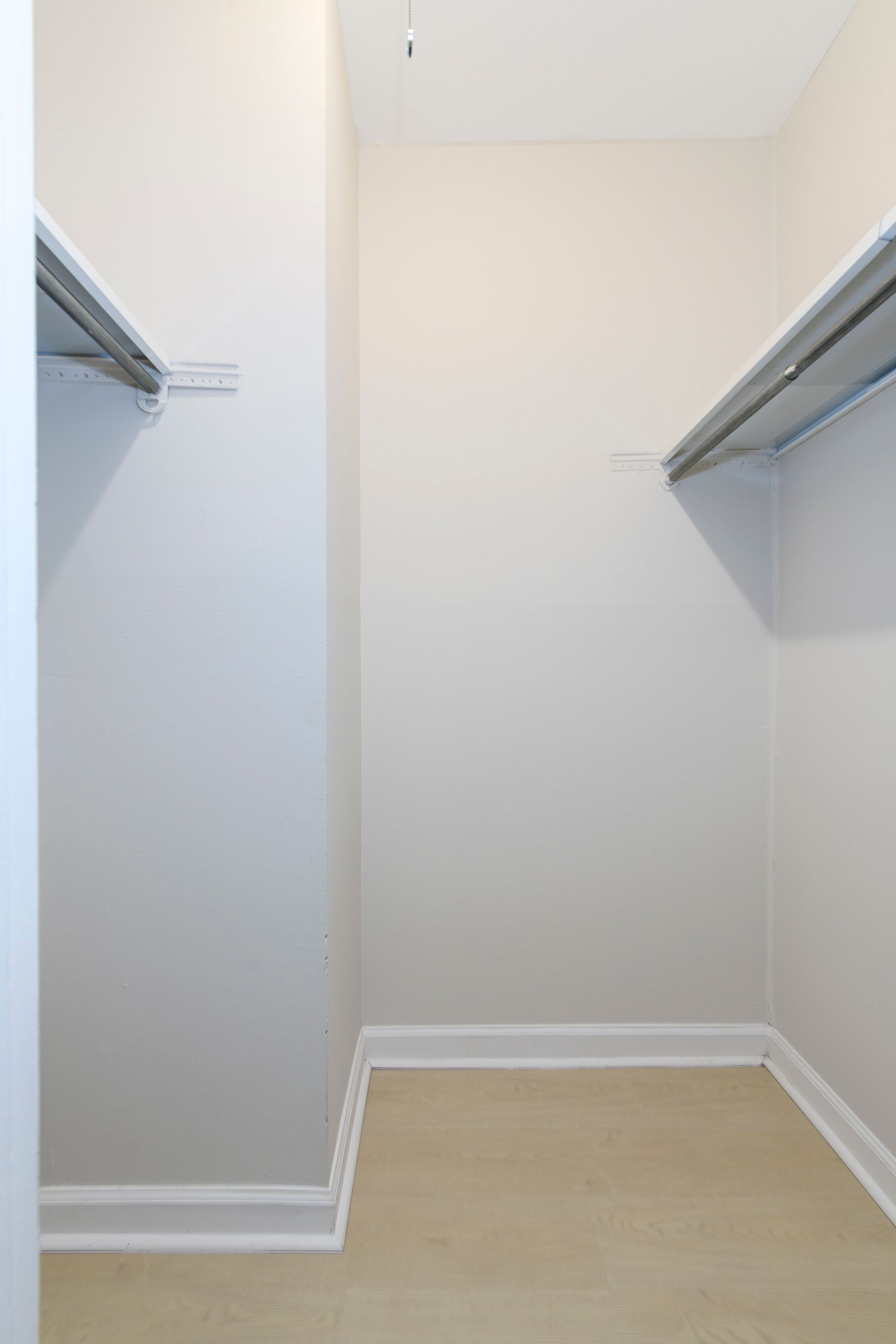 Empty walk-in closet with shelves and tan carpet. Beige walls and white trim.