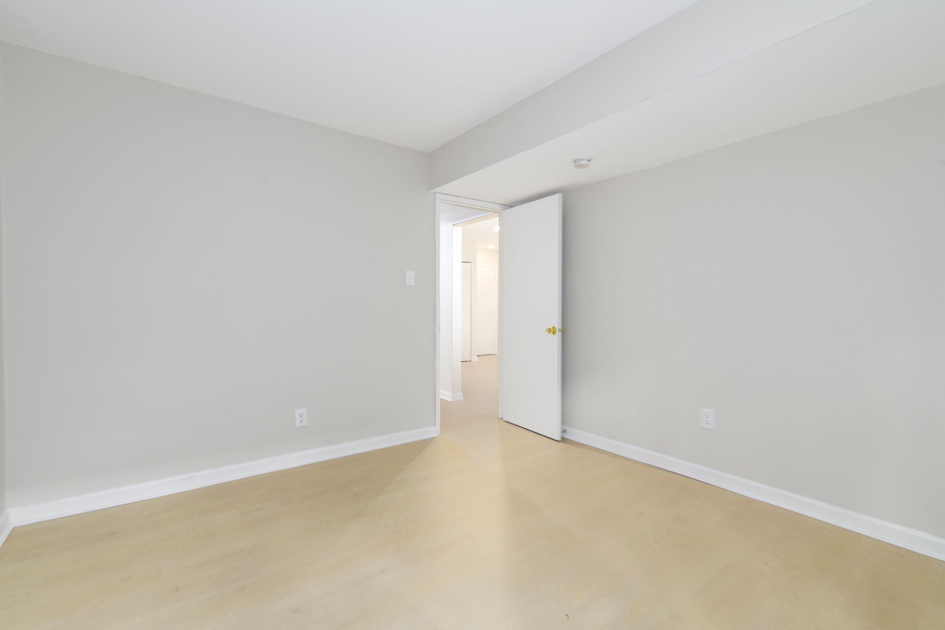 Empty room with light gray walls, white trim, and beige floor. An open doorway leads to a hallway.