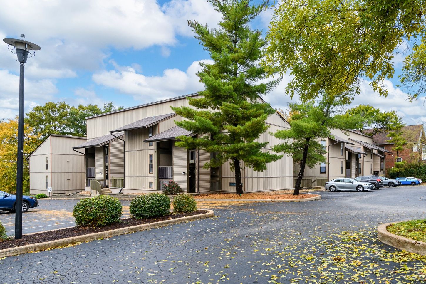 Exterior view of a beige building with a parking lot and trees on a partly cloudy day.