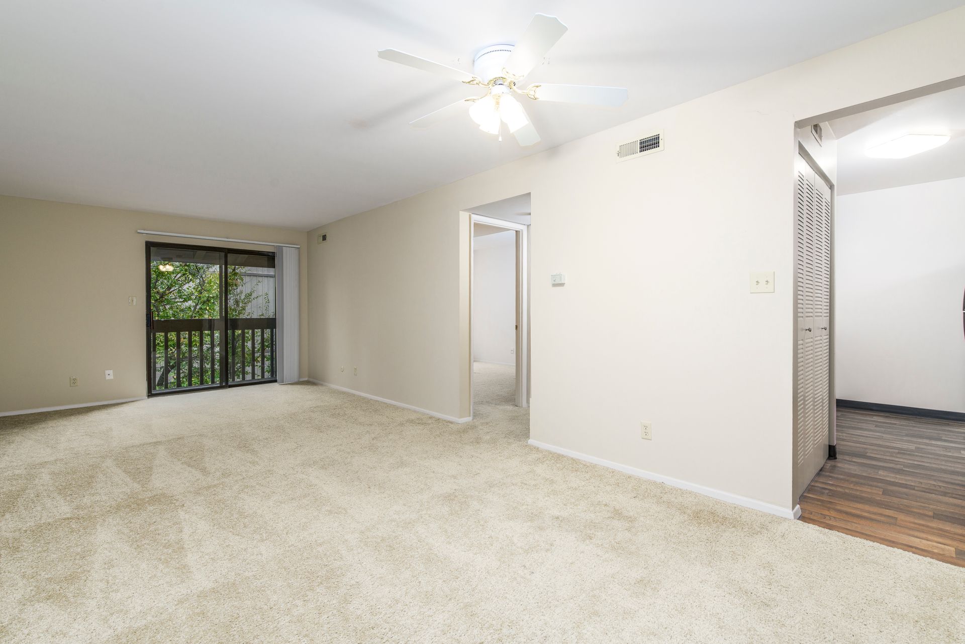 Empty living room with beige walls, carpet, and a sliding glass door to a balcony.