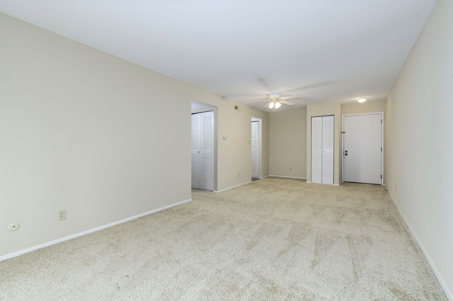 Empty room with beige carpet and walls, three doorways, and a ceiling fan.